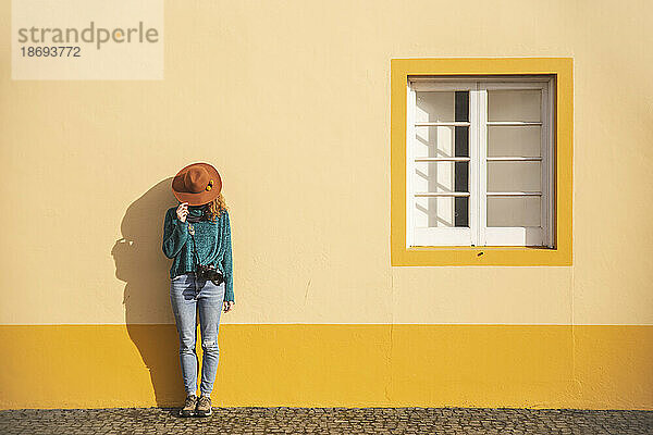 Frau mit Hut und Kamera steht vor der Wand