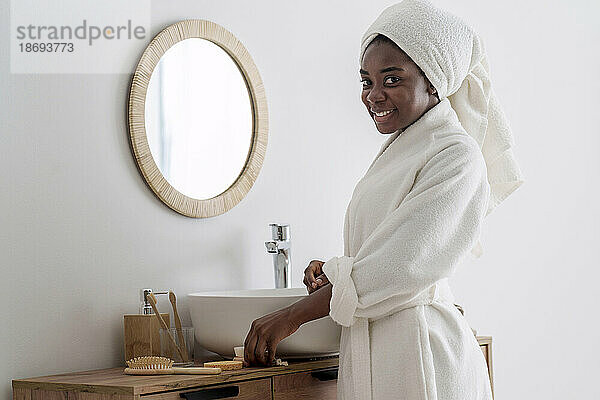 Smiling woman wearing bathrobe standing in bathroom at home
