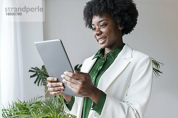 Glückliche junge Geschäftsfrau  die im Büro einen Tablet-PC nutzt