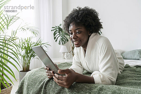Smiling woman using tablet PC lying on bed at home