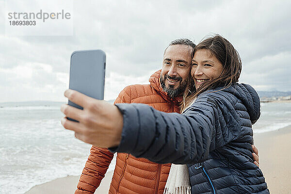 Glückliche Frau macht Selfie mit reifem Mann am Strand