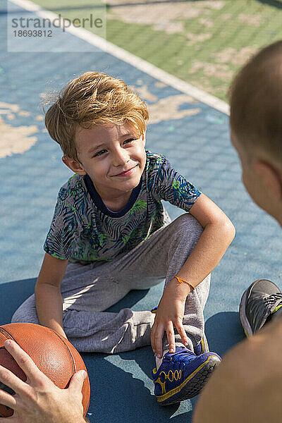 Lächelnder Sohn sitzt mit Vater am Sportplatz