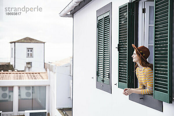 Frau mit Hut lehnt am Fenster