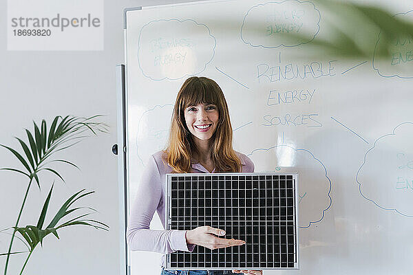 Lächelnde Geschäftsfrau mit Solarpanel vor dem Whiteboard