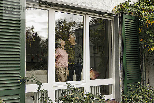 Älteres Paar hinter der Fensterscheibe ihres Hauses
