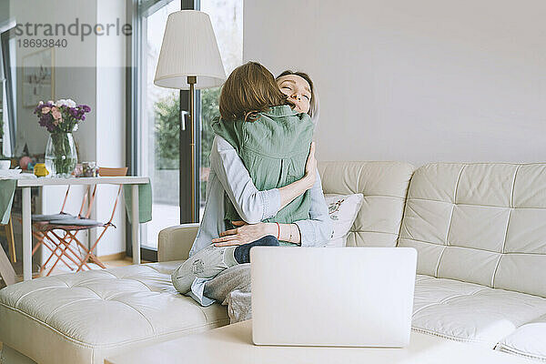 Mother hugging son sitting on sofa at home