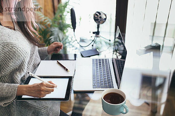 Podcaster nutzt Tablet-PC und Laptop am Schreibtisch zu Hause