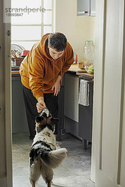 Nicht-binäre Person füttert Hund in der heimischen Küche
