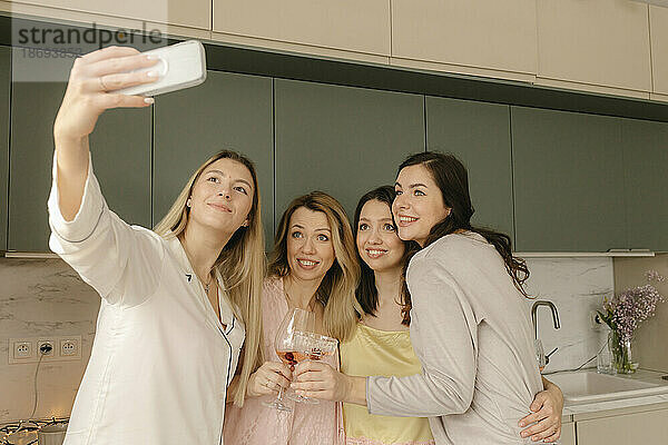 Frau macht Selfie per Smartphone mit Freunden in der heimischen Küche