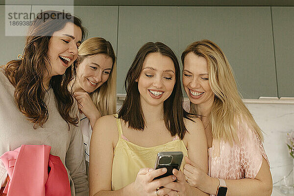 Lächelnde Frau  die zu Hause ihr Mobiltelefon mit Freunden teilt