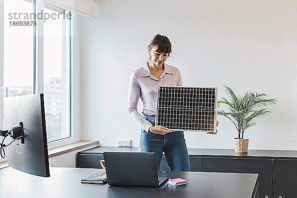 Lächelnde Geschäftsfrau mit Solarpanel spricht per Videoanruf über Laptop