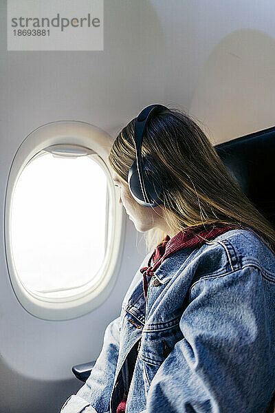 Frau mit Kopfhörern schaut im Flugzeug aus dem Fenster