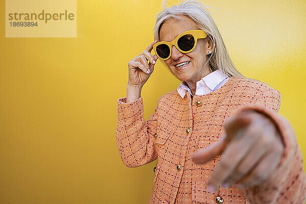 Lächelnde Frau mit Sonnenbrille vor gelber Wand