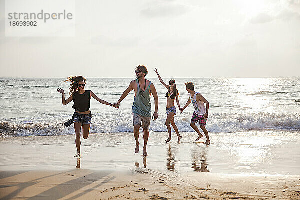 Fröhliche Freunde halten Händchen und spielen am Strand