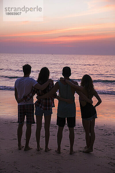 Freunde mit Armen und Blick auf den Sonnenuntergang am Strand