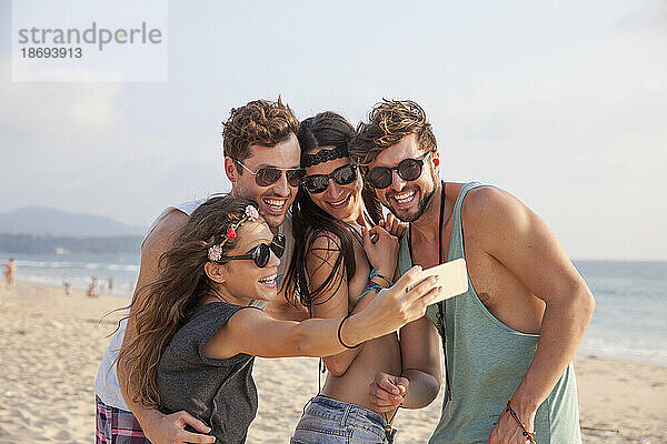Glückliche Frau  die im Urlaub am Strand ein Selfie mit Freunden macht