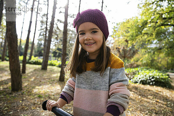 Lächelndes Mädchen mit Strickmütze hält Fahrradgriff im Park