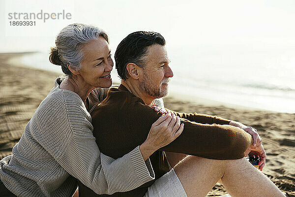 Lächelnde Frau umarmt Mann  der am Strand sitzt