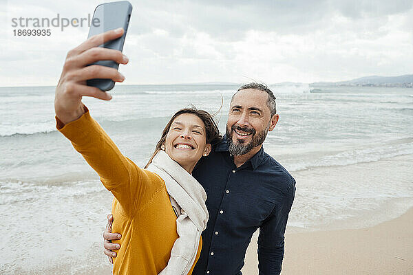 Glückliche Frau macht Selfie mit Mann per Handy am Strand