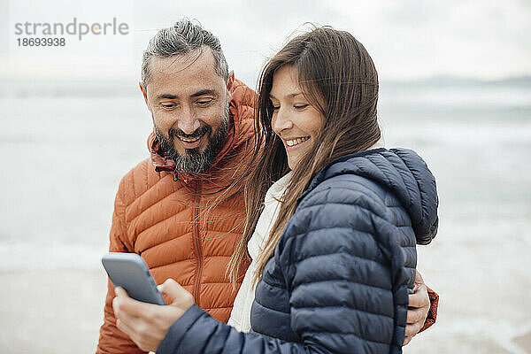Glücklicher Mann und Frau  die am Strand ihr Smartphone benutzen