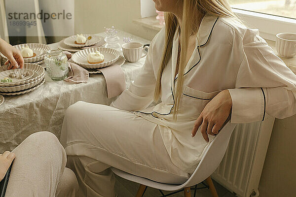 Frau im Schlafanzug sitzt zu Hause auf einem Stuhl am Esstisch