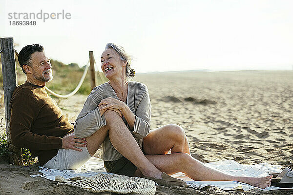 Glückliche Frau  die mit einem Mann spricht  der am Strand sitzt