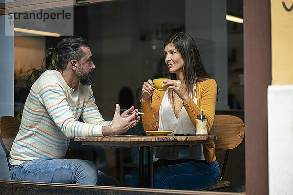 Ein Mann unterhält sich mit einer Frau  die im Café sitzt und durch die Glasscheibe eine Tasse sieht