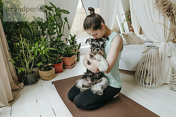Frau küsst Schnauzer-Hund  der zu Hause auf einer Trainingsmatte sitzt
