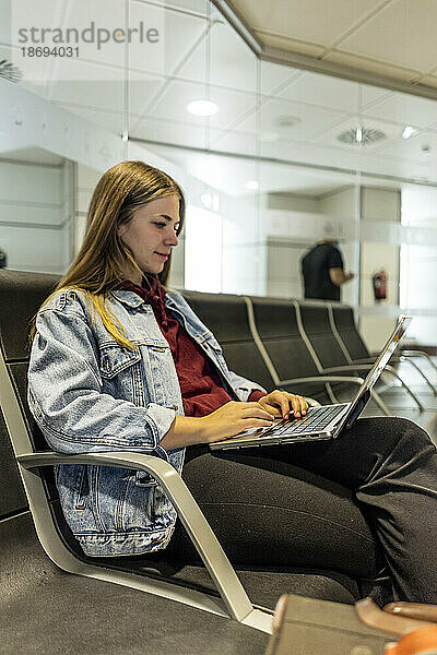 Frau sitzt mit Laptop auf Sitzplatz am Flughafen