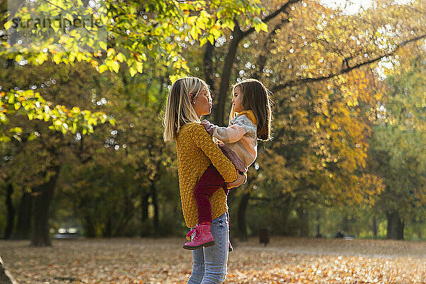 Mutter trägt Tochter im Arm im Herbstpark