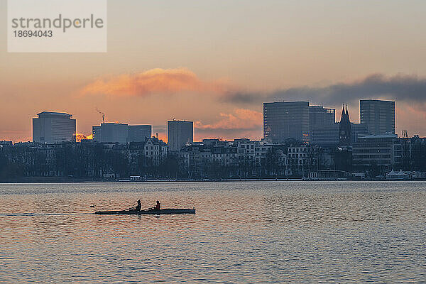 Deutschland  Hamburg  Alster im Morgengrauen mit Skyline der Stadt und Ruderboot im Hintergrund