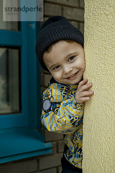 Smiling cute boy peeking from wall