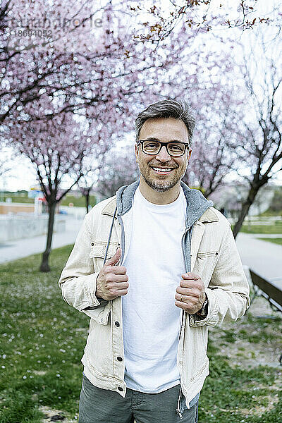 Lächelnder Mann mit Brille steht im Park