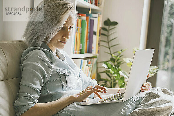 Frau benutzt Laptop auf Sofa zu Hause