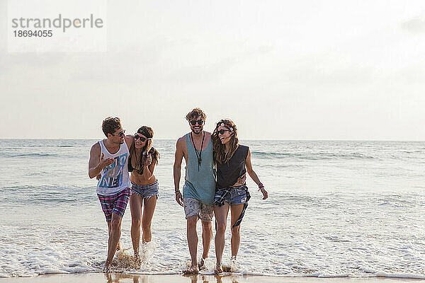 Glückliche Freunde  die am Strand im Wasser spazieren gehen