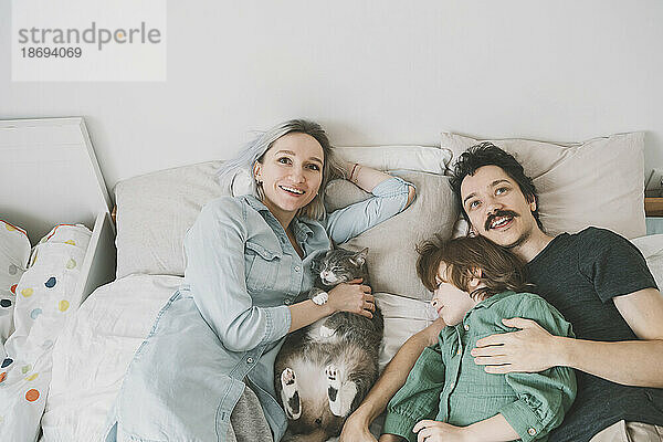 Happy family with cat relaxing on bed at home