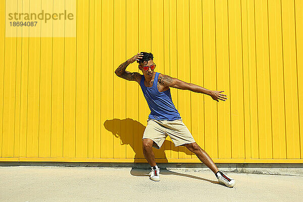Junger Mann tanzt an einem sonnigen Tag vor einer gelben Wand
