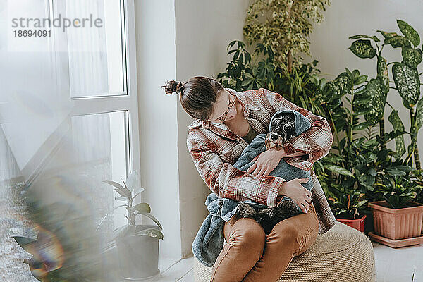 Frau umarmt in Handtuch gewickelten Schnauzer-Hund zu Hause