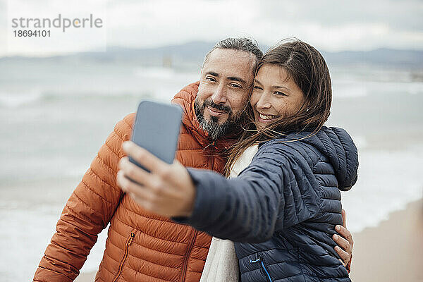 Glückliche Frau macht Selfie mit Mann per Smartphone am Strand