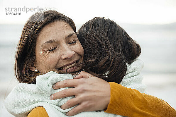 Glückliche Frau umarmt Tochter am Strand