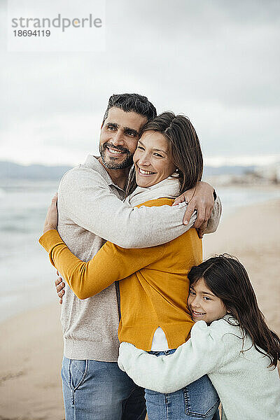Glücklicher Mann und Frau mit Tochter  die sich am Strand umarmen