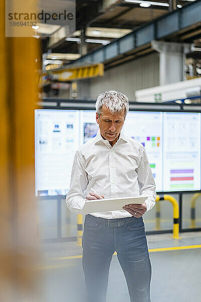 Geschäftsmann steht und benutzt Tablet-PC in der Fabrik