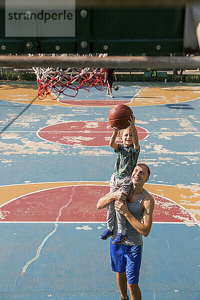 Glücklicher Vater und Sohn spielen Basketball auf dem Sportplatz