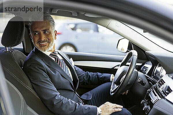 Lächelnder Geschäftsmann sitzt auf dem Fahrersitz im Auto