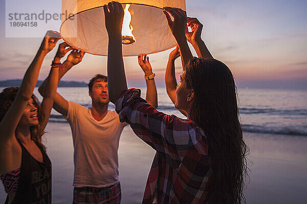 Frau hält brennende Papierlaterne mit Freunden am Strand