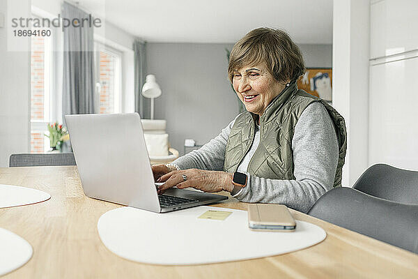Lächelnde Frau  die zu Hause einen Laptop auf dem Tisch benutzt