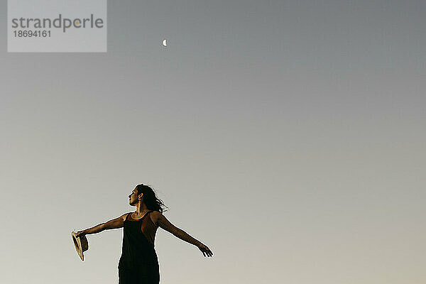 Frau steht mit ausgestreckten Armen unter einem Himmel mit Mond