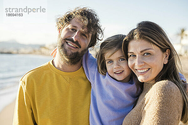 Glückliche Eltern mit süßer Tochter am Strand