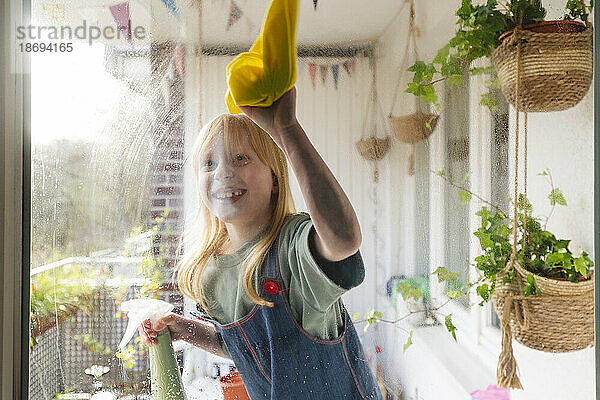 Fröhliches Mädchen putzt Glasfenster vom Balkon aus