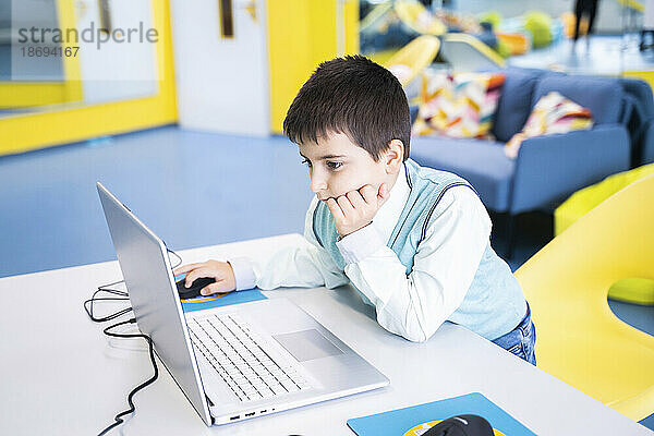 Konzentrierter Junge benutzt Laptop am Schreibtisch im Computerunterricht